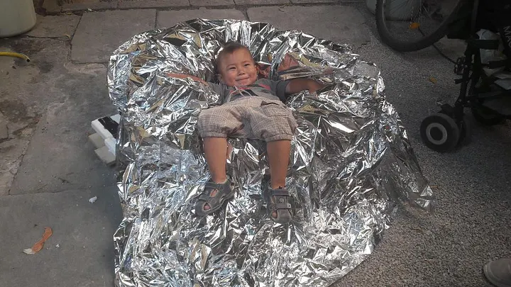 Un enfant migrant joue sur l’un des cuiseurs solaires fabriqués lors d’un atelier low-tech à Lesbos — © Juin 2018, Pascaline Roi